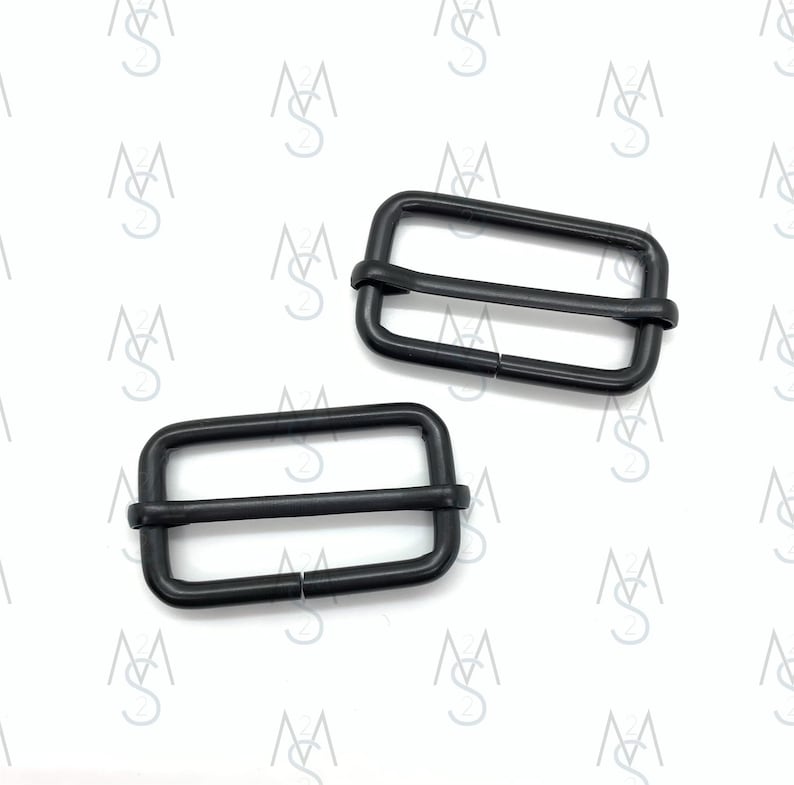 May include: Two black metal slider buckles. The buckles are rectangular with two parallel bars. The buckles are commonly used for straps, bags, and other accessories.