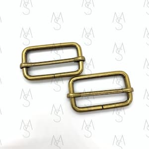 May include: Two gold-toned metal slider buckles. The buckles are rectangular with a smooth, slightly textured surface.