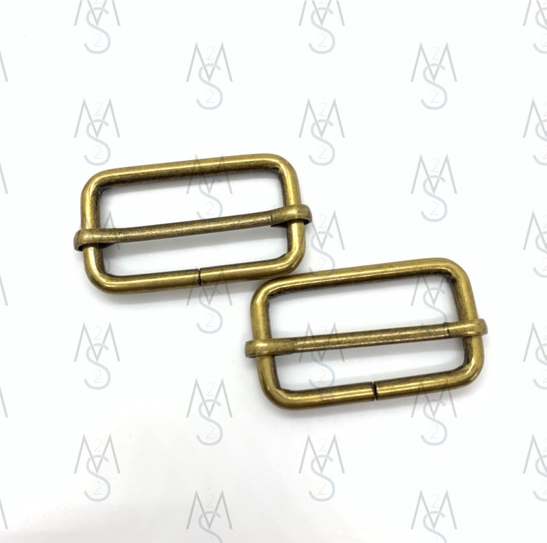 May include: Two gold-toned metal slider buckles. The buckles are rectangular with a smooth, slightly textured surface.