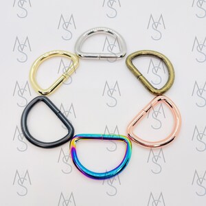 May include: Six different colored metal D-rings. The rings are silver, gold, bronze, black, rose gold, and rainbow.