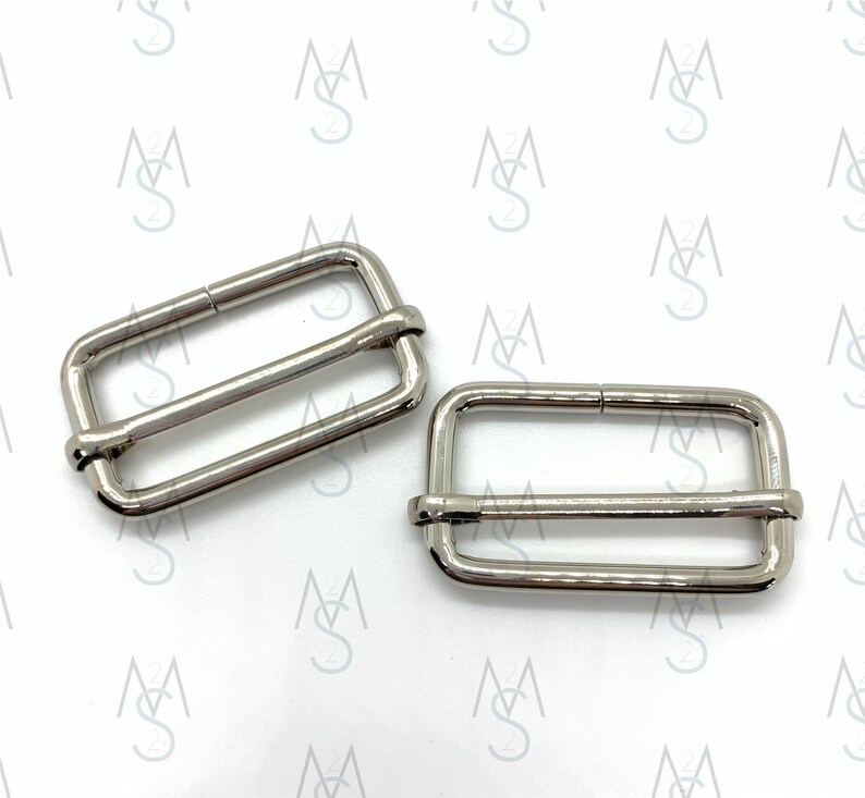 May include: Two silver metal slider buckles for straps or belts. The buckles are rectangular with a smooth finish.
