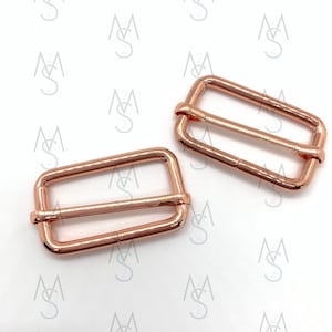 May include: Two rose gold metal slider buckles. The buckles are rectangular with a smooth finish.
