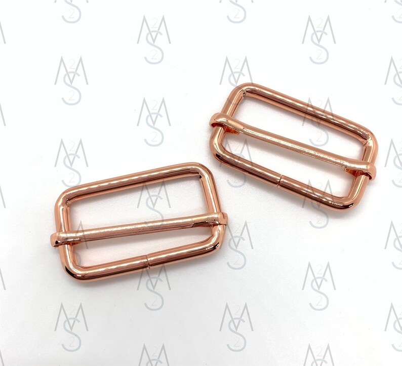 May include: Two rose gold metal slider buckles. The buckles are rectangular with a smooth finish.