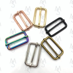 May include: Six metal slider buckles in different colors: rose gold, gold, black, rainbow, silver, and antique brass. The buckles are all the same size and shape, with a rectangular frame and a center bar.
