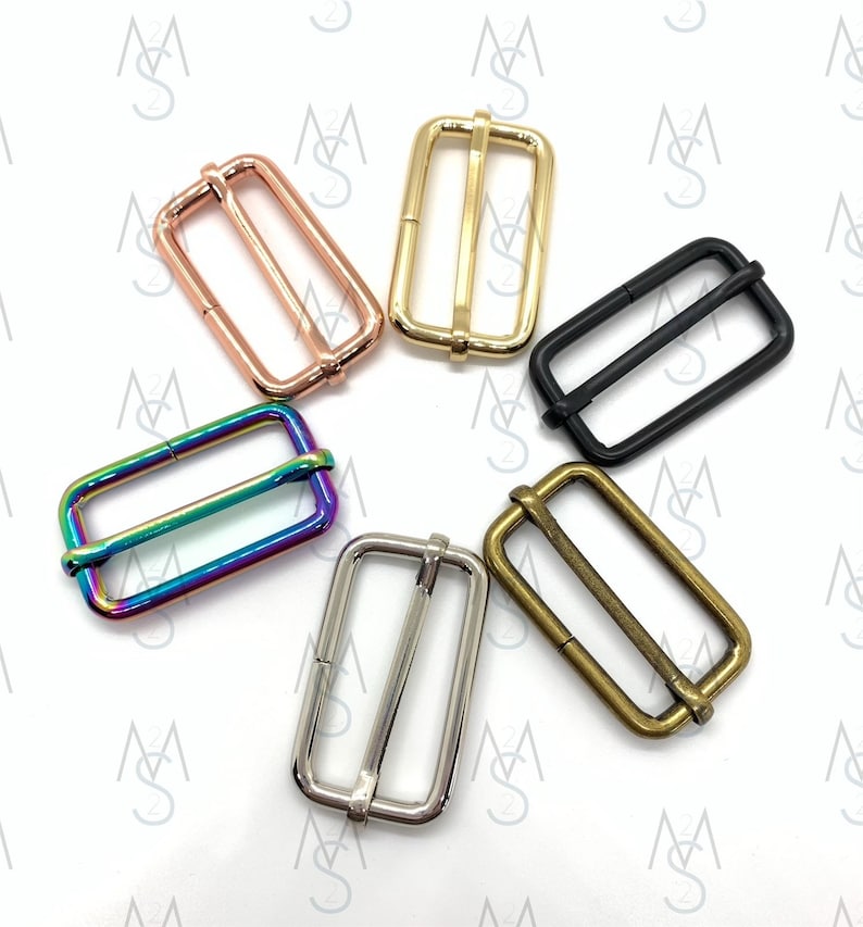 May include: Six metal slider buckles in different colors: rose gold, gold, black, rainbow, silver, and antique brass. The buckles are all the same size and shape, with a rectangular frame and a center bar.