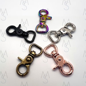 May include: Five different metal swivel clasps in various finishes: black, iridescent, silver, antique brass, and rose gold. These clasps are commonly used for attaching straps, leashes, or other accessories.