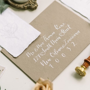 May include: A brown envelope with white calligraphy that reads "Mr. & Mrs. Thomas Rene 127 South Main Street New Orleans, Louisiana 70032".