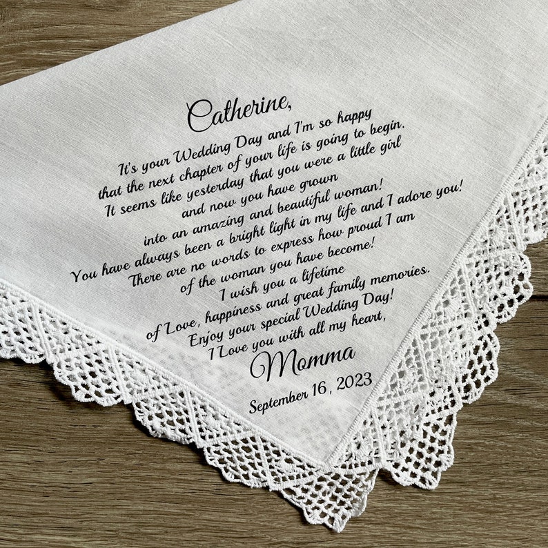 Może przedstawiać: Biała chusteczka z delikatną, szydełkową koronkową obw&oacute;dką. Chusteczka zawiera odręczną wiadomość i imię "Catherine" w eleganckim skrypcie, wraz z datą "16 września 2023". Sentimentalna pamiątka ślubna.