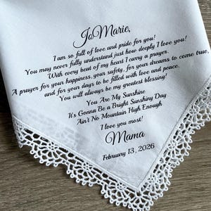 Może przedstawiać: Biała chusteczka z delikatną koronkową lam&oacute;wką i czarnym pismem. Tekst zawiera miłosne przesłanie, imię "Jo Marie" i datę 13 lutego 2026 r. Sentimentalna pamiątka.