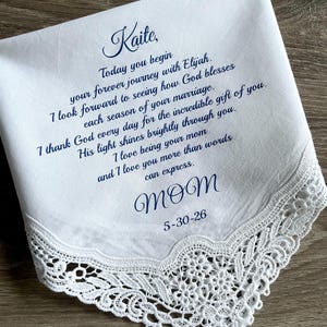 May include: White handkerchief with delicate lace trim. The handkerchief has blue script that reads "Kaite" and a heartfelt message from "Mom" with the date 5-30-26. A sentimental keepsake.