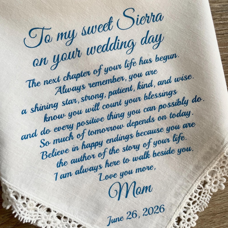 May include: White handkerchief with blue script, including the text "To my sweet Sierra on your wedding day." The handkerchief has a delicate lace trim and a message from "Mom," dated June 26, 2026.