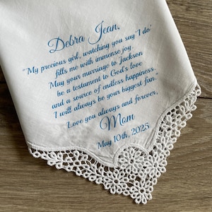 May include: White handkerchief with delicate lace trim and blue script. The text reads "Debra Jean" followed by a heartfelt message from "Mom" and the date "May 10th, 2025". A sentimental keepsake.