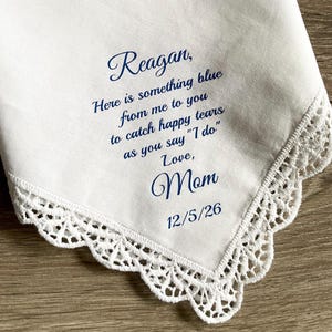 May include: White handkerchief with a delicate lace trim. The handkerchief has blue text that reads "Reagan, Here is something blue from me to you to catch happy tears as you say "I do" Love, Mom 12/5/26."