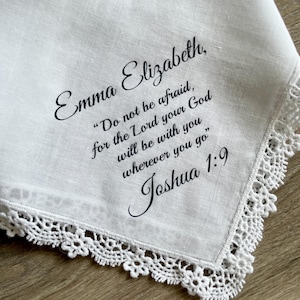 May include: White handkerchief with a delicate lace trim. The handkerchief features the name "Emma Elizabeth" and a quote from Joshua 1:9 in elegant script. A thoughtful and personalized gift.