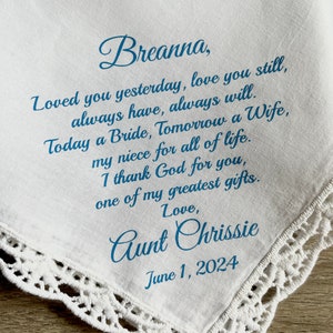 May include: White handkerchief with blue text. The text reads "Breanna, Loved you yesterday, love you still... Aunt Chrissie June 1, 2024." The handkerchief has a delicate lace trim.