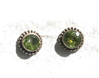 Puede incluir: Un par de pendientes de plata con detalles de piedras preciosas verdes. Los pendientes tienen forma redonda y un borde de cuentas.