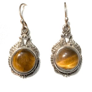 May include: A pair of silver earrings with a brown tiger's eye stone in each. The earrings have a delicate, ornate design.