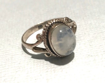 May include: A silver ring featuring a white oval moonstone set in a delicate, ornate design.