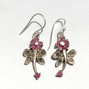 May include: A pair of silver dangle earrings featuring a dragonfly design with pink gemstone accents.