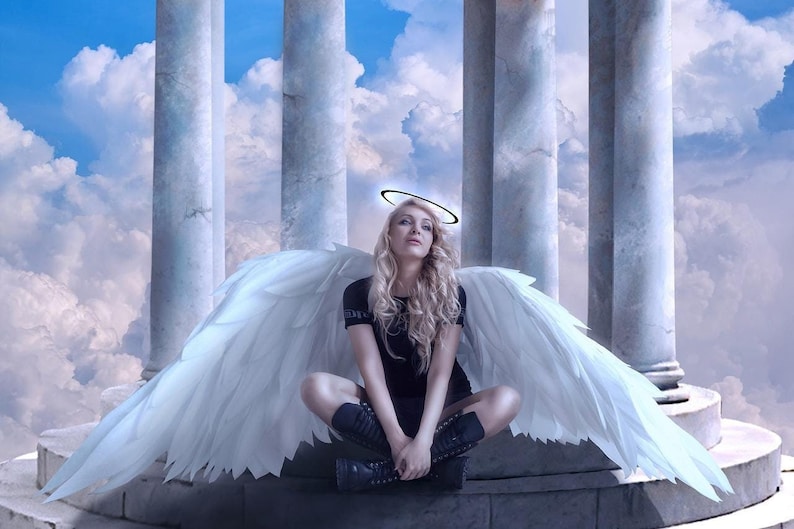 May include: A woman with long blonde hair, wearing a black top and boots, sits with large white feathered wings spread behind her. A halo is above her head. The background features white columns and a cloudy sky.