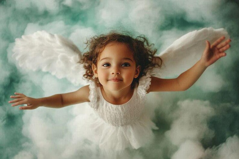 May include: A young child with curly brown hair and brown eyes, wearing a white dress and feathery wings, appears to be floating in a cloudy, teal-colored sky. The child's arms are outstretched, and she is smiling.
