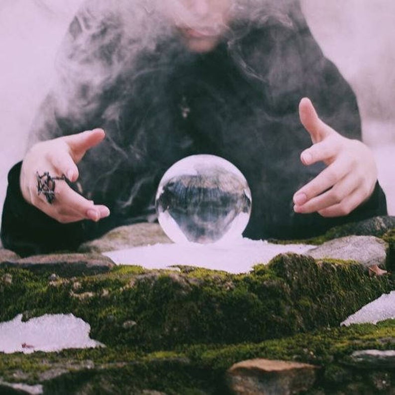 May include: A clear crystal ball, resting on a moss-covered stone surface, with a person's hands hovering over it. Wisps of smoke or vapor surround the ball, creating an ethereal atmosphere. The scene evokes themes of fortune-telling and mysticism.