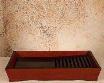 May include: A rectangular wooden tray with a reddish-brown exterior finish. The interior features a flat, solid dark brown section on the left and a slatted dark brown drainage grate on the right, designed with a low-profile, open-top structure.