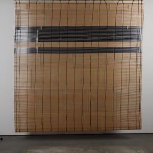 Könnte beinhalten: Ein natürlicher Bambus-Rollladen mit schwarzen horizontalen Streifen. Der Rollladen besteht aus dünnen, vertikalen Bambuslamellen, die durch schwarzen Faden zusammengehalten werden. Die schwarzen Streifen befinden sich oben am Rollladen.