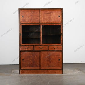 Könnte beinhalten: Ein Holzschrank in Rotbraun mit Schiebetüren und Schubladen. Der Schrank hat einen dunkelbraunen Rahmen und Griffe. Er verfügt über Glasböden und sichtbare Holzmaserung. Der Schrank ist rechteckig und mit "EASTERN CLASSICS" beschriftet.