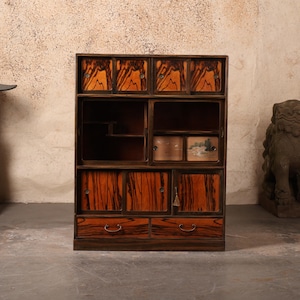 Könnte beinhalten: Ein Vintage-Holzschrank mit mehreren Fächern und Schubladen. Der Schrank weist ein auffälliges Holzmaserungsmuster in Braun- und Rotbrauntönen auf. Er hat eine rechteckige Form mit einer Kombination aus geschlossenen Türen und offenen Regalen.