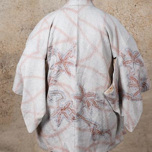 May include: A white and light pink kimono with a floral pattern. The kimono has a traditional Japanese design with a wide collar and long sleeves.