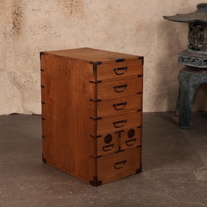 May include: A wooden cabinet with six drawers, featuring a warm brown finish and dark metal corner reinforcements. Each drawer has a D-shaped handle. The cabinet is a piece of furniture.