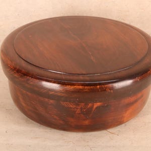 Puede incluir: Una caja redonda de madera con tapa. La caja está hecha de madera marrón oscura y tiene un acabado liso.