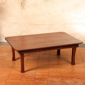 May include: A low-profile rectangular wooden table featuring a smooth, dark brown surface with rounded corners and four sturdy, slightly curved legs. The table is constructed from solid wood with a visible grain pattern and a polished finish.