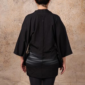 May include: A black kimono with a subtle striped pattern. The kimono has long sleeves and a relaxed fit.