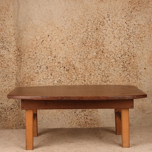 May include: A low wooden coffee table with a dark brown rectangular top featuring rounded corners and straight edges. The table is supported by four light-colored wooden legs that are connected to the underside of the tabletop frame.