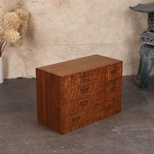 May include: A small wooden dresser with six drawers. The dresser is made of a light brown wood with a unique grain pattern. The drawer pulls are dark metal. The top of the dresser is a darker shade of brown.