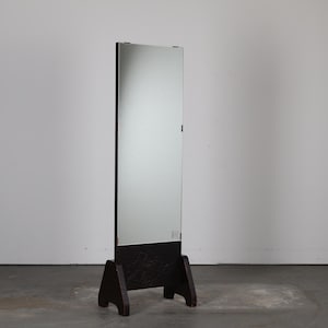 以下が含まれることがあります： ダークブラウンの木製フレームとベースが付いた、長方形の全身鏡。ベースには彫刻された花の模様があります。鏡は2本足のベースの上に立っており、部屋を映しています。鏡の高さは約152cmです。