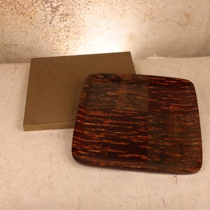 May include: A square tray with a dark brown, mottled wood grain pattern featuring a smooth, polished finish. Positioned behind the tray is a rectangular, solid olive-green box with a flat surface and clean, straight edges.