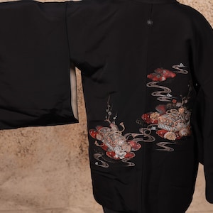 May include: A black kimono with a traditional Japanese design featuring red, gold, and white floral motifs. The kimono has long sleeves and a relaxed fit.