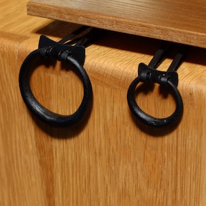 May include: Two black metal rings attached to a wooden surface. The rings are different sizes and have a simple, elegant design.