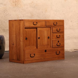 May include: A wooden cabinet with a dark brown finish. It has two doors with a decorative design and six drawers with black metal handles.