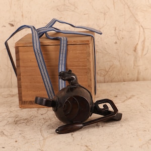 May include: A dark brown, antique-style wooden tea set with a rat figurine on top. The set includes a teapot, a spoon, and a wooden box with a blue and white striped strap.