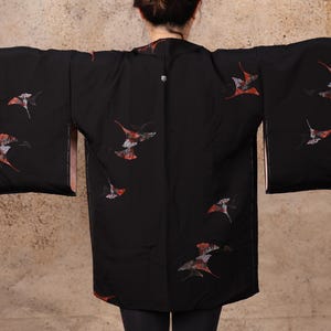 May include: A black kimono with a pattern of red and white birds. The kimono has long sleeves and a wide collar.
