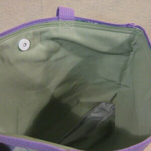 Puede incluir: Vista interior de un bolso tote morado con interior verde. El bolso tiene asas y ribetes morados. Se ve un cierre magn&eacute;tico blanco. La tela interior es de color verde liso.