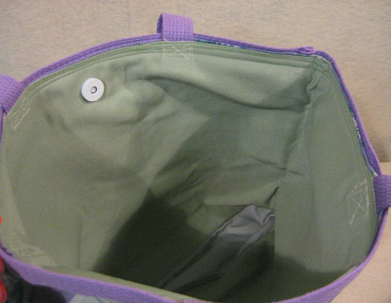 Puede incluir: Vista interior de un bolso tote morado con interior verde. El bolso tiene asas y ribetes morados. Se ve un cierre magn&eacute;tico blanco. La tela interior es de color verde liso.
