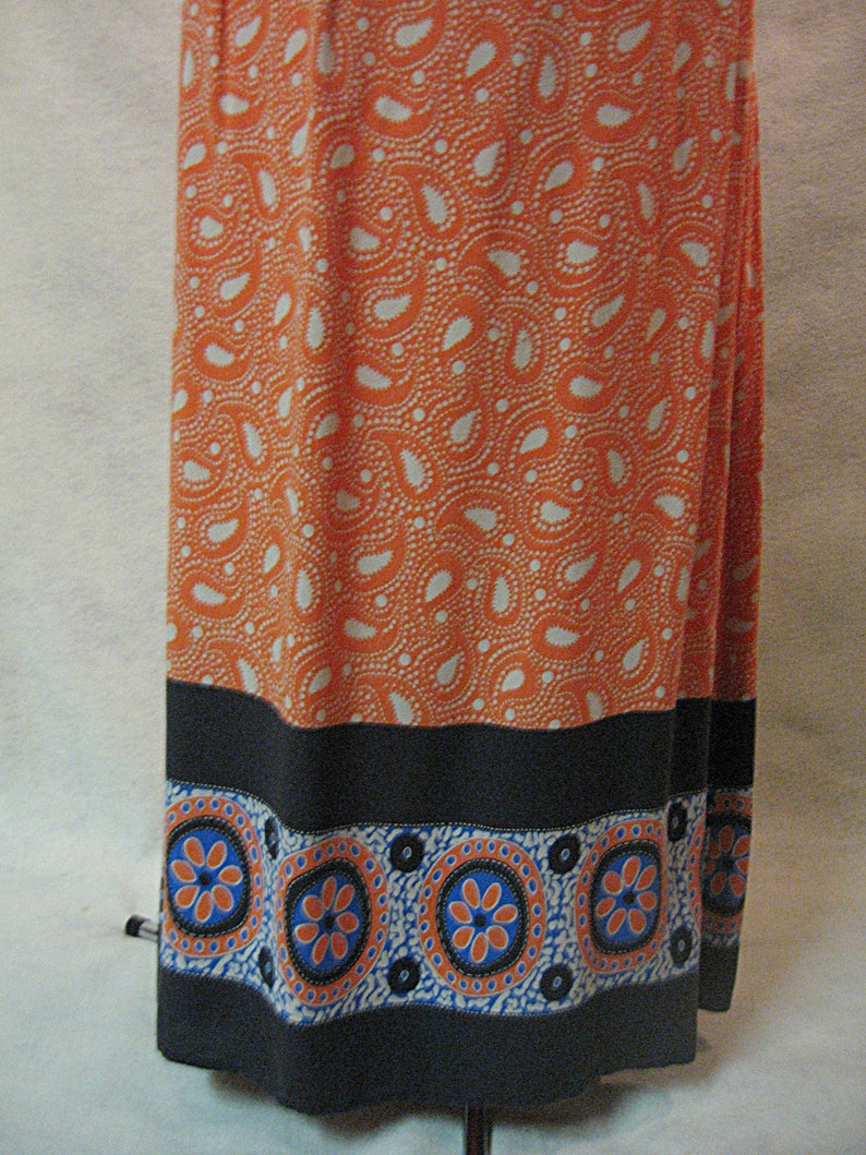 Pu&ograve; includere: Una lunga gonna arancione con un motivo paisley bianco e un bordo nero e bianco con disegni floreali blu e arancioni.