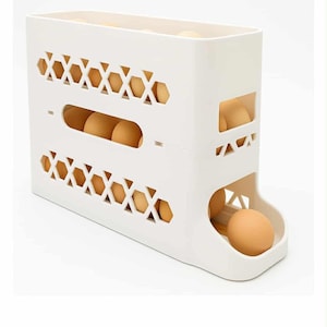 May include: A white plastic egg storage container with a two-tiered design. The container has decorative cutouts and holds several brown eggs. The bottom tier has a dispensing slot for easy access to the eggs.