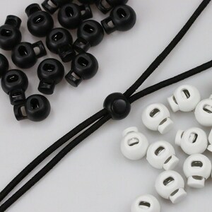 May include: A close-up of black and white plastic cord ends. There are 18 black cord ends and 15 white cord ends. The cord ends are round with a hole in the centre.