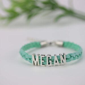 May include: A braided turquoise leather bracelet with a silver charm that spells out the name "MEGAN".